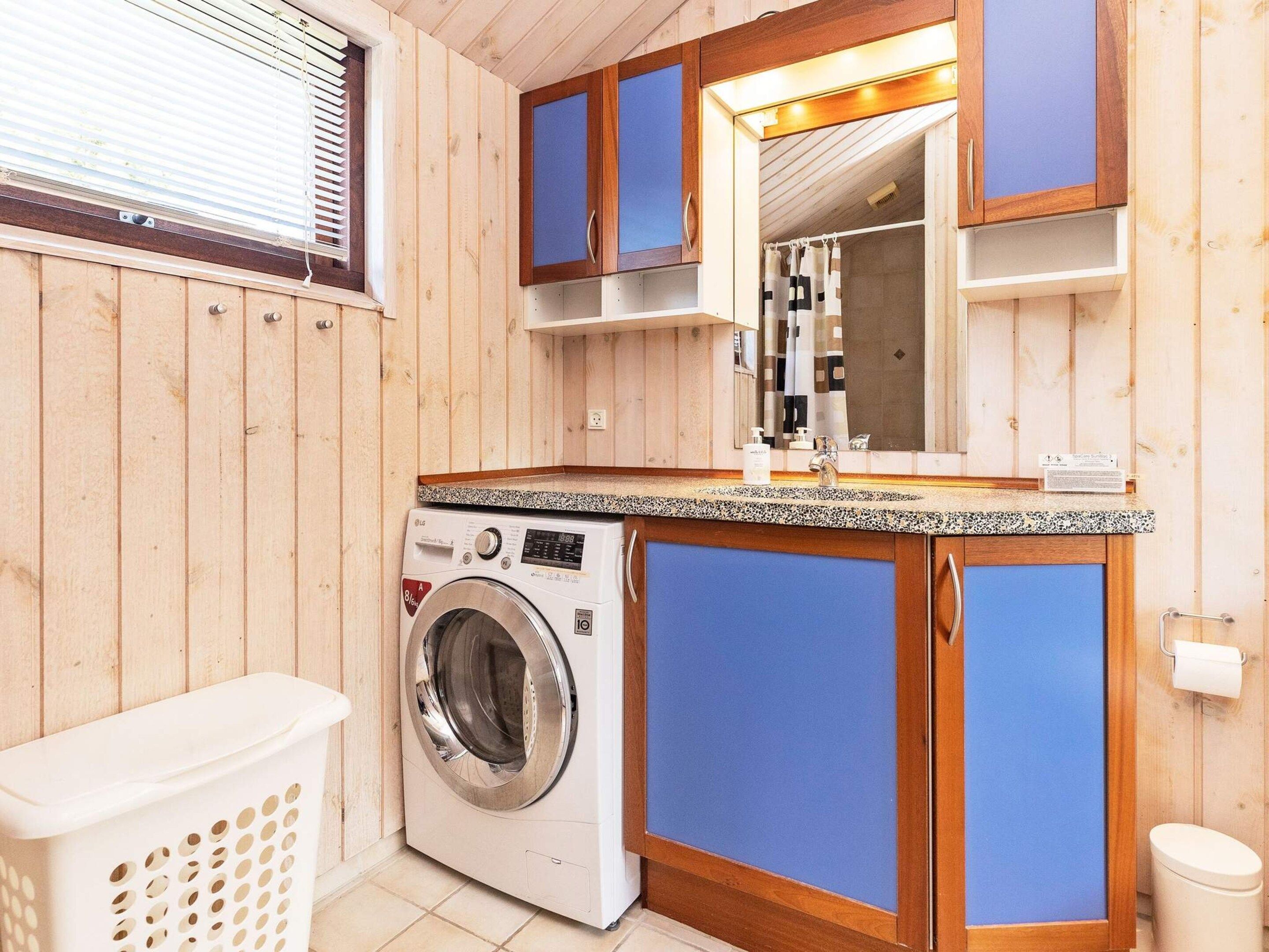 A compact bathroom with wooden paneling, a washing machine, a sink with a mirror, and a toilet.