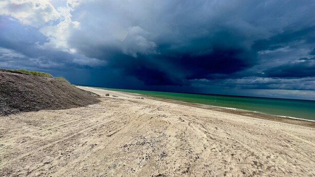 A beach with a sandy foreground and a stormy sky.