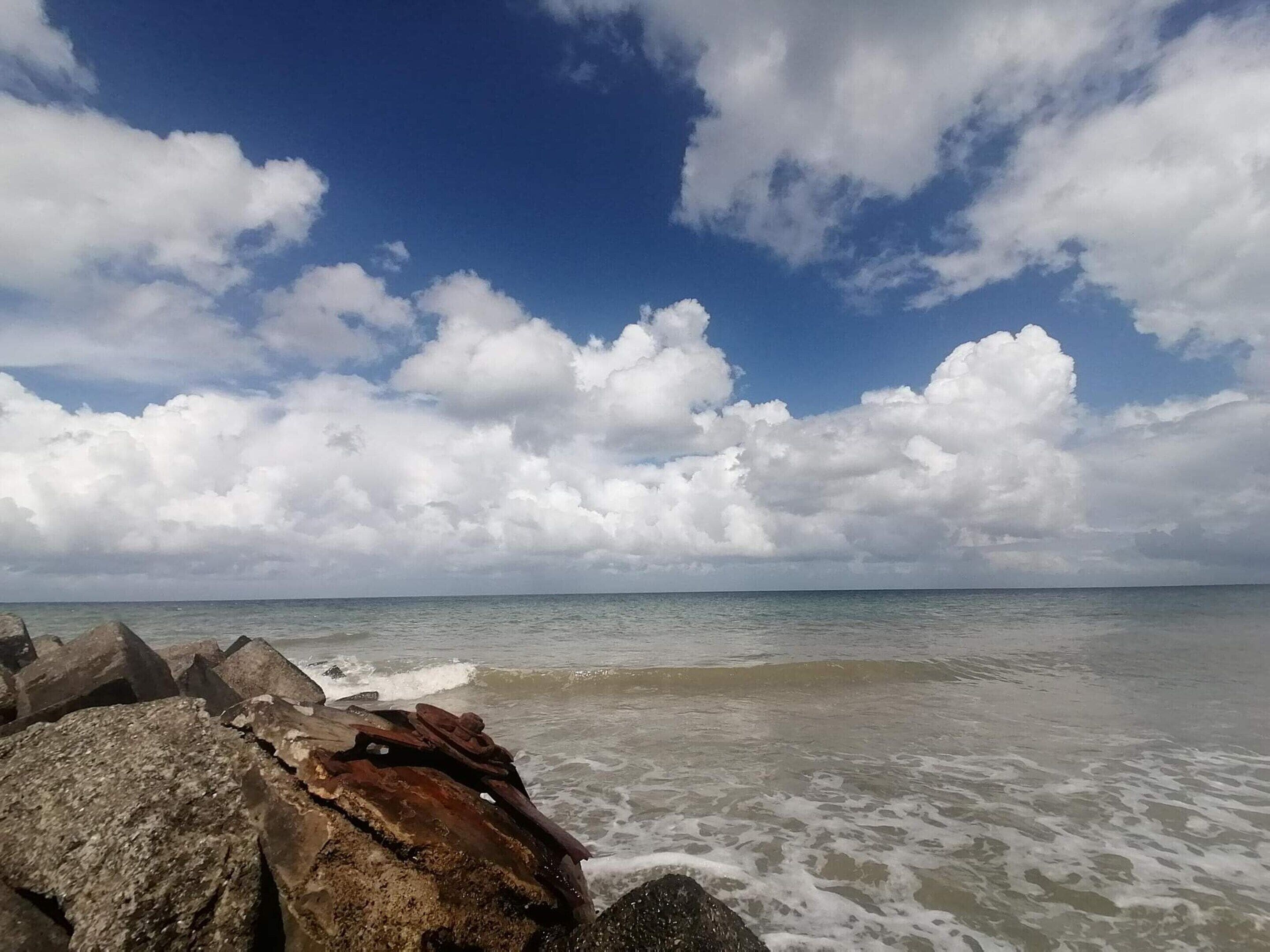 Une plage avec de gros rochers au premier plan et un ciel dégagé parsemé de nuages.
