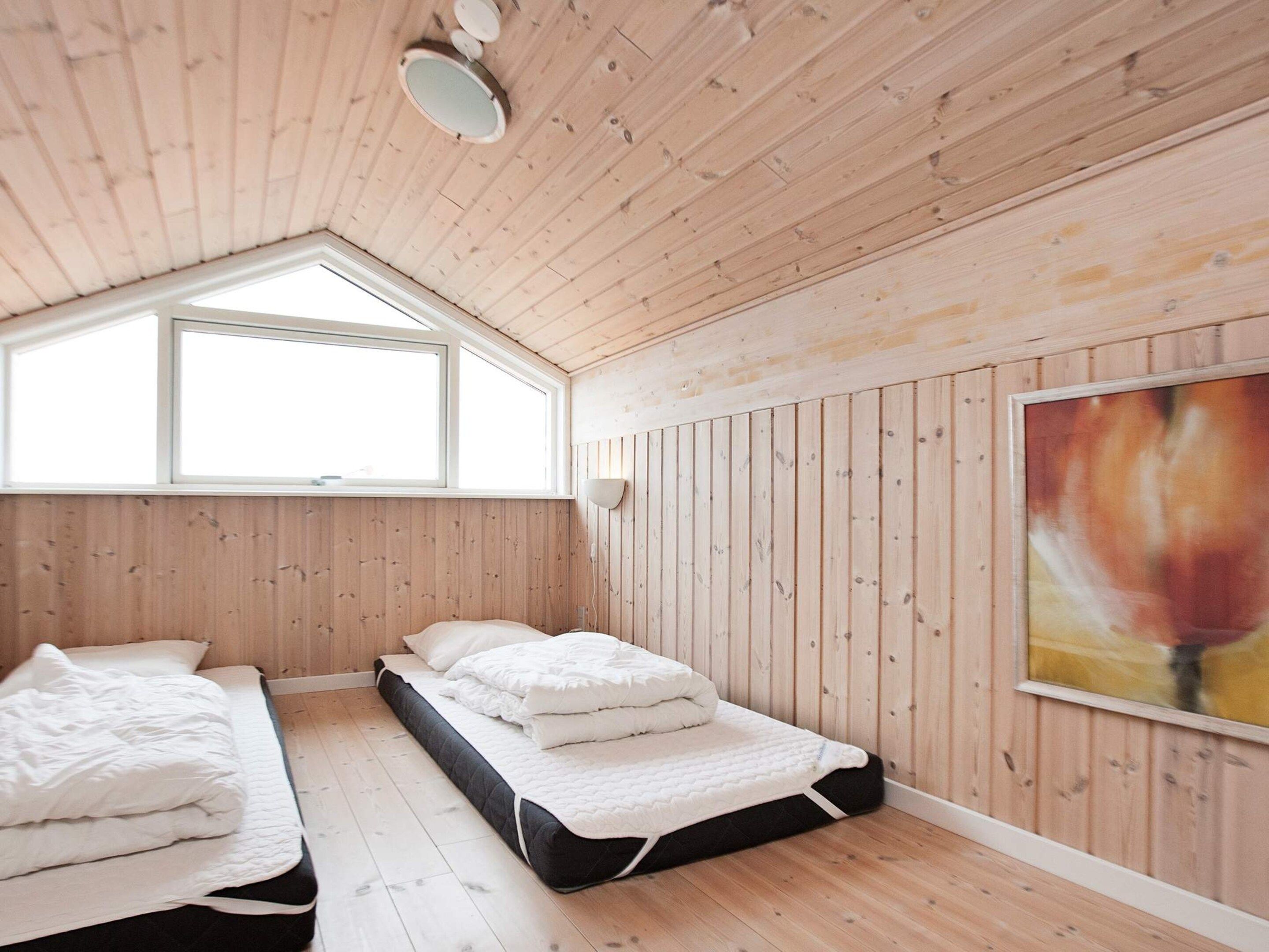 A room with two beds, wooden walls, a sloped ceiling, and a large window.