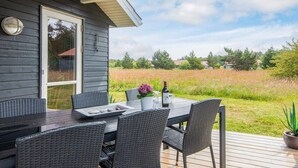 A covered outdoor dining area with a table and chairs, a potted plant, and a bottle of wine. - Picturesque Holiday Home in Ulfborg near Sea (Ulfborg)