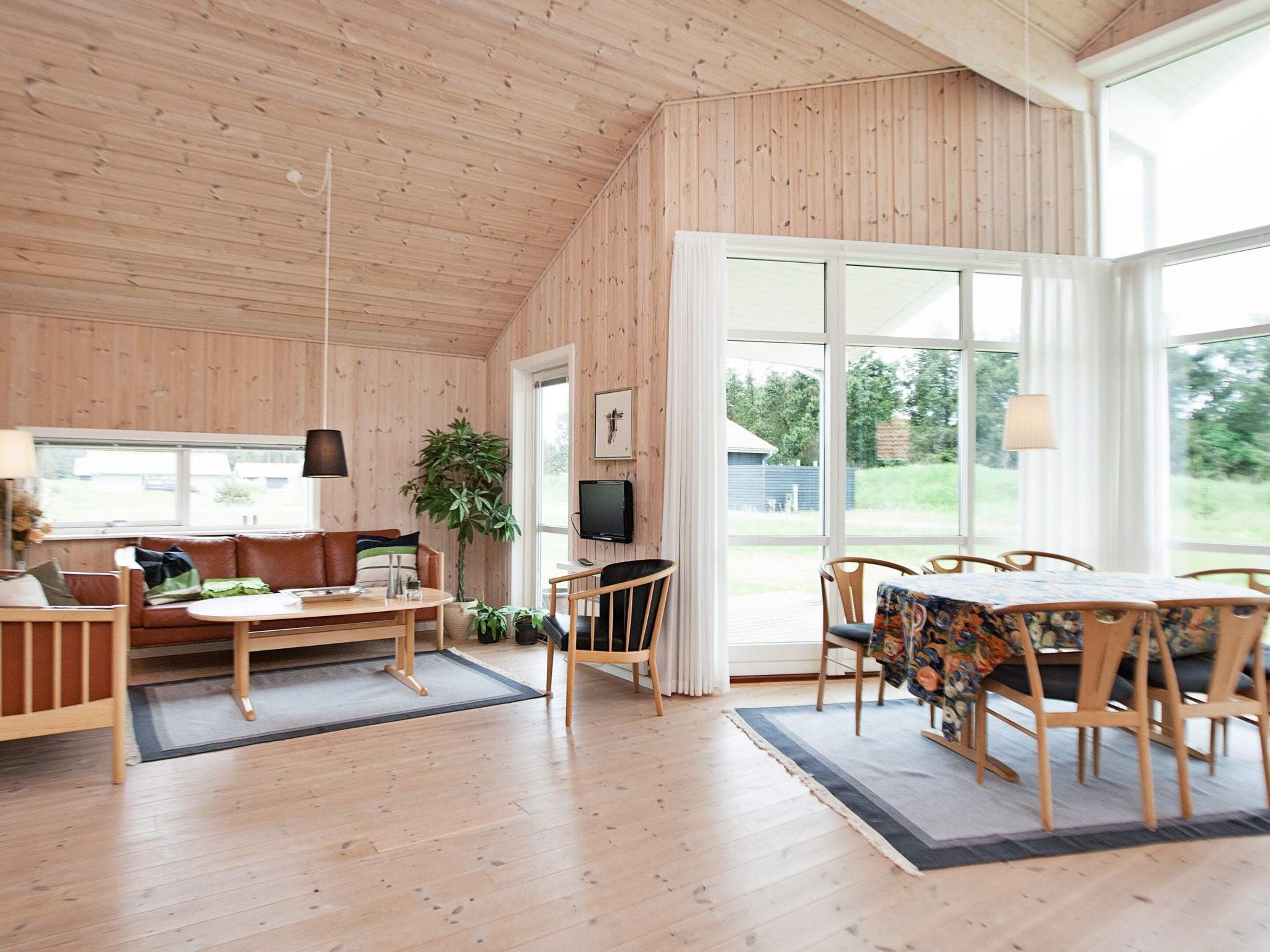 Une pièce spacieuse avec un plancher en bois, un canapé, une table à manger avec des chaises, un téléviseur et de grandes fenêtres.