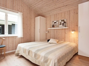 A bedroom with a bed, a chair, a wardrobe, and a shelf with pictures. - Picturesque Holiday Home in Ulfborg near Sea (Ulfborg)