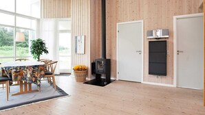 A spacious room with wooden walls, a large window, a dining table with chairs, a fireplace, and a television. - Picturesque Holiday Home in Ulfborg near Sea (Ulfborg)