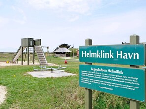 A playground with a slide and climbing structure, a small shelter, and a sign indicating 'Helmklink Havn'.