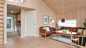 A spacious living area with a wooden floor, a brown leather sofa, a wooden coffee table, and a dining table. There is a door leading to a kitchen and a balcony. - Picturesque Holiday Home in Ulfborg near Sea (Ulfborg)