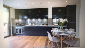 Uma cozinha moderna com armários escuros, uma ilha central e uma área de refeições com mesa e cadeiras.