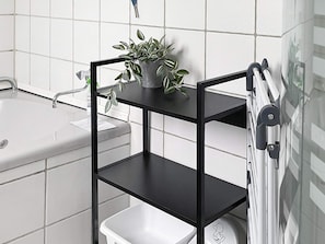 A bathroom with a black metal shelf holding a potted plant, a white sink, and a toilet.