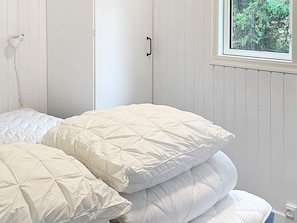 A bedroom with a bed, white walls, a window with a view of trees, and a door with a handle.