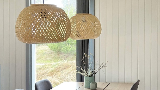 Ein Essbereich mit einem Holztisch, zwei gewebten Pendelleuchten und einer Pflanzvase.