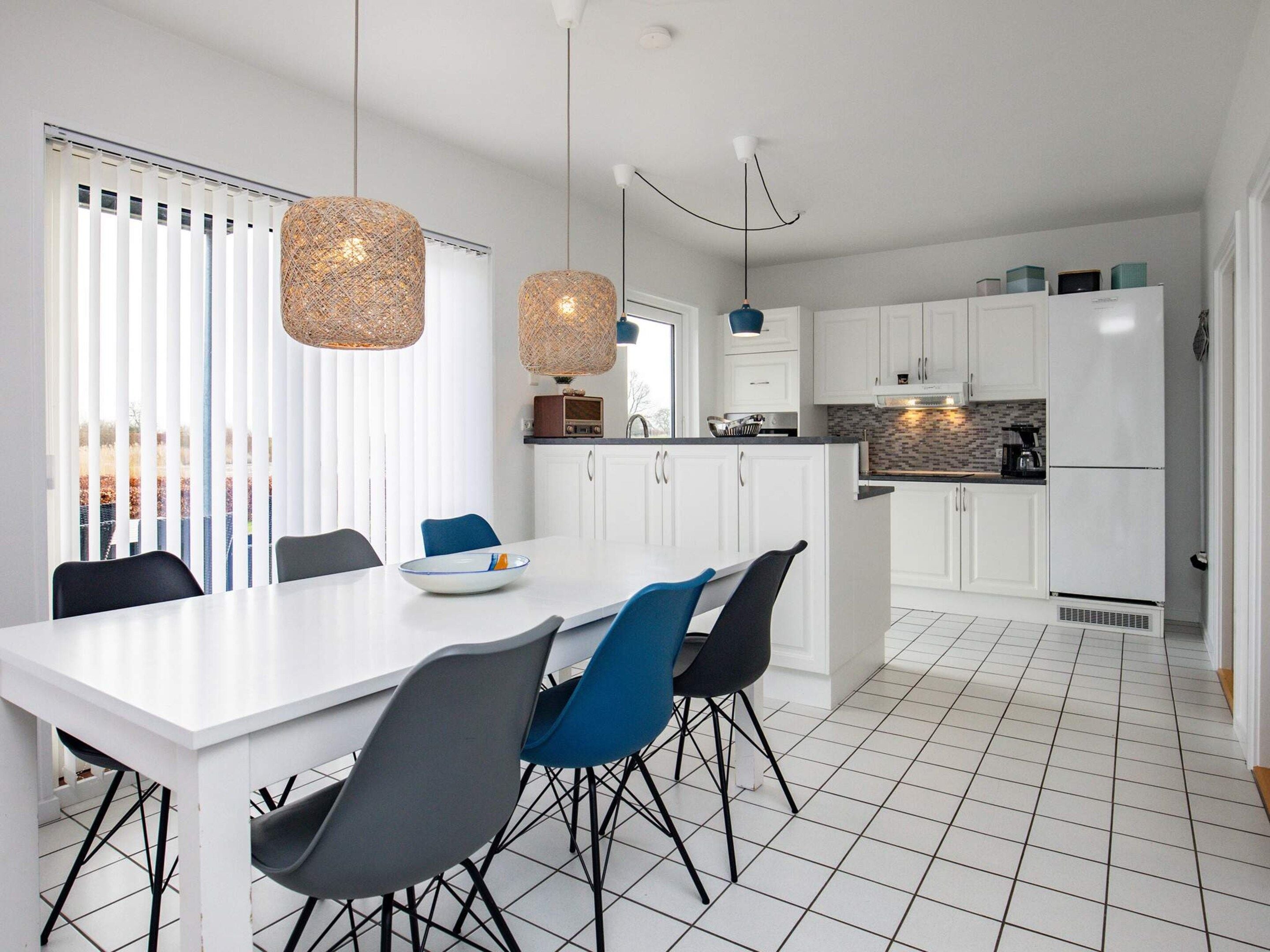 A modern kitchen with white cabinets, a central island, and a dining area with a white table and chairs.