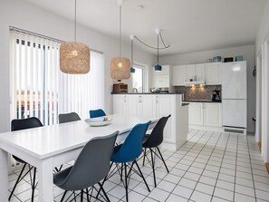 Cocina moderna con armarios blancos, una isla central y un área de comedor con mesa y sillas blancas.