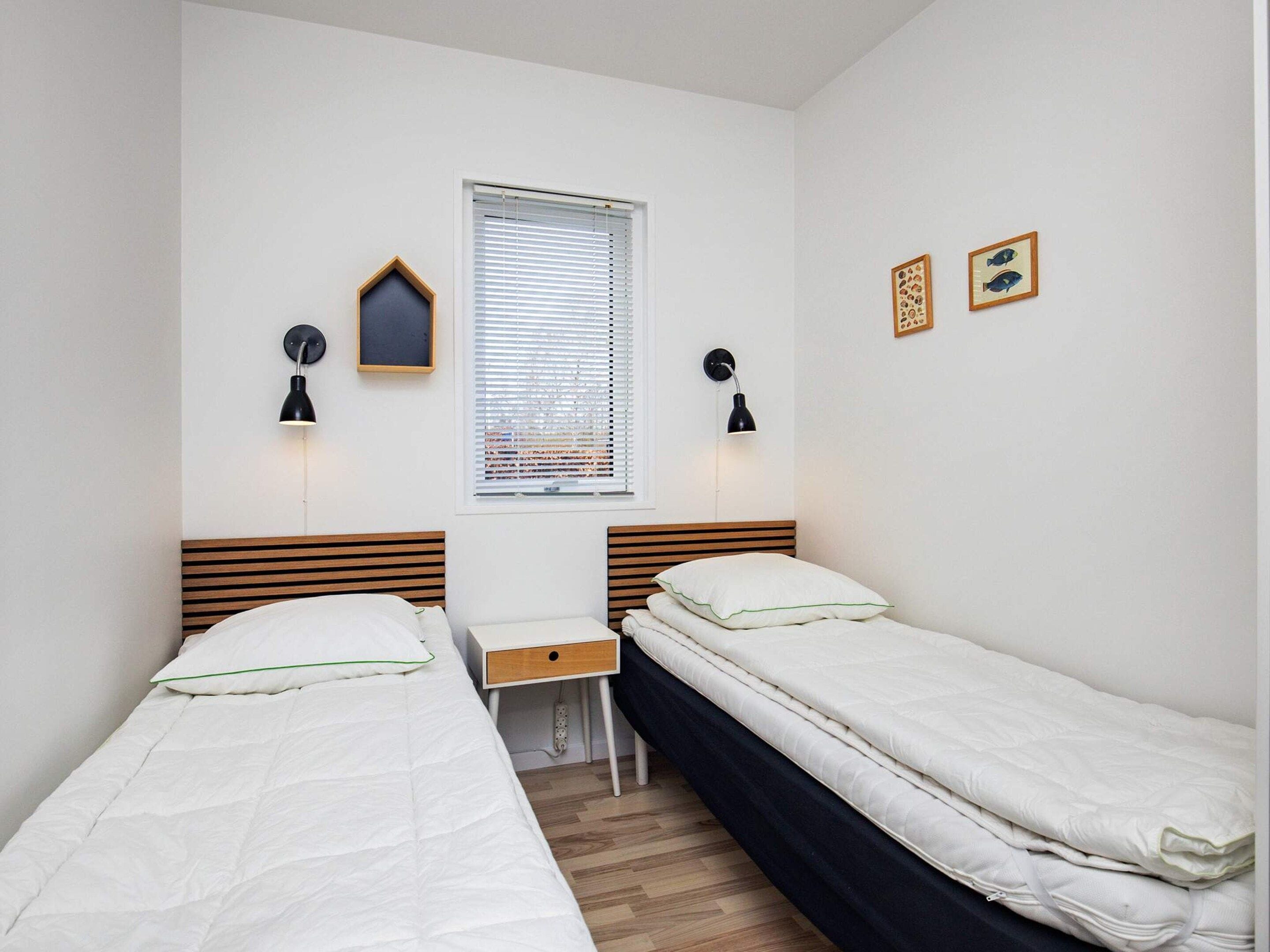 A bedroom with two single beds, a desk, and two wall-mounted lamps.