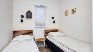 A bedroom with two single beds, a desk, and two wall-mounted lamps.