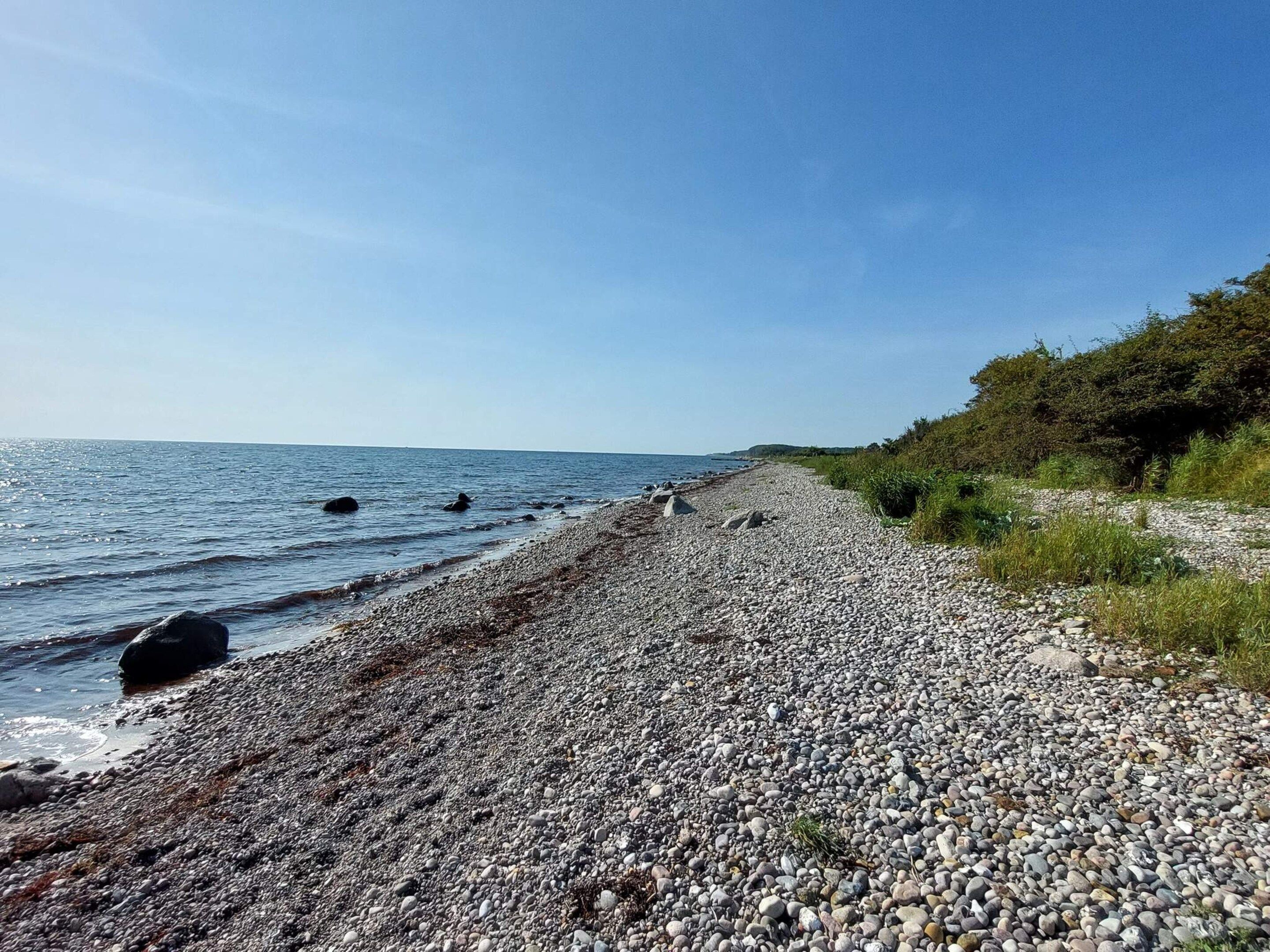 A pebbled beach with a clear sky and calm sea.