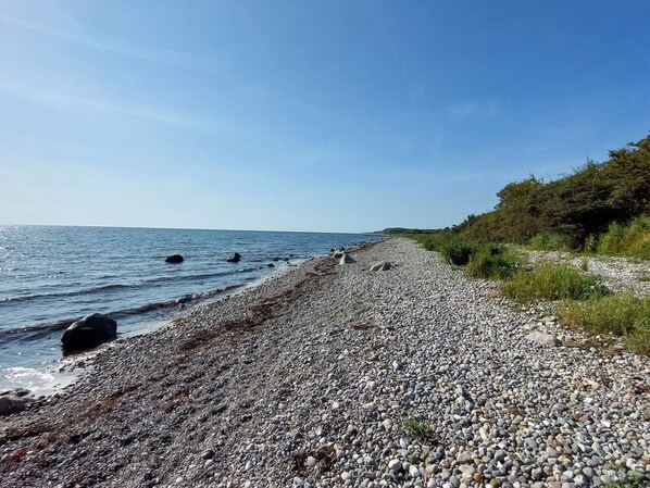 A pebbled beach with a clear sky and calm sea.
