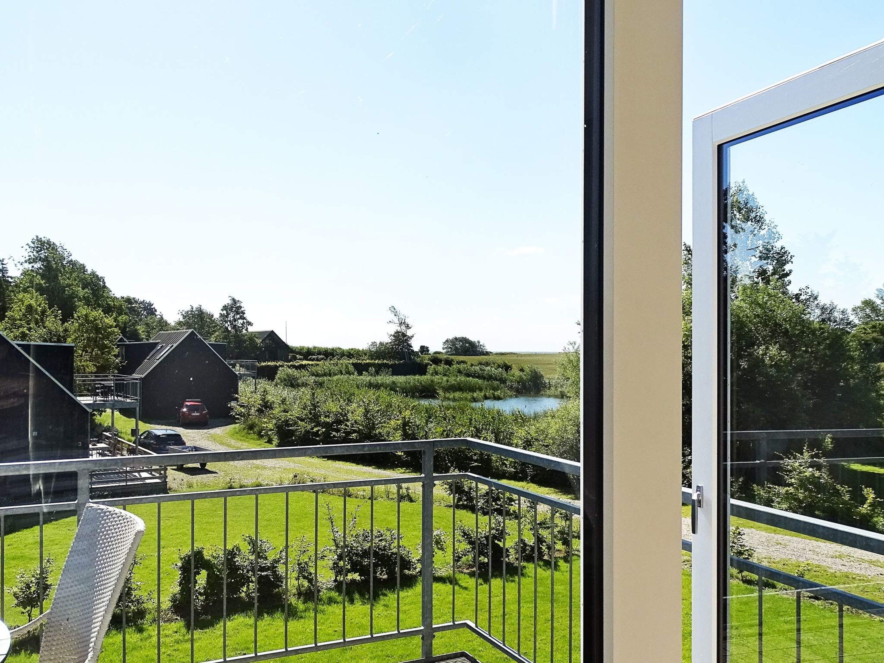 A balcony with a view of a green landscape, a body of water, and a building in the distance.
