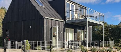 Une maison moderne à deux étages, dotée d’un balcon, d’un espace extérieur clôturé et d’un mur en pierre.