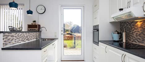 A modern kitchen with white cabinets, a black countertop, a visible clock, and a view through the door.