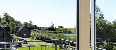 A balcony with a view of a grassy area, a body of water, and buildings in the distance.