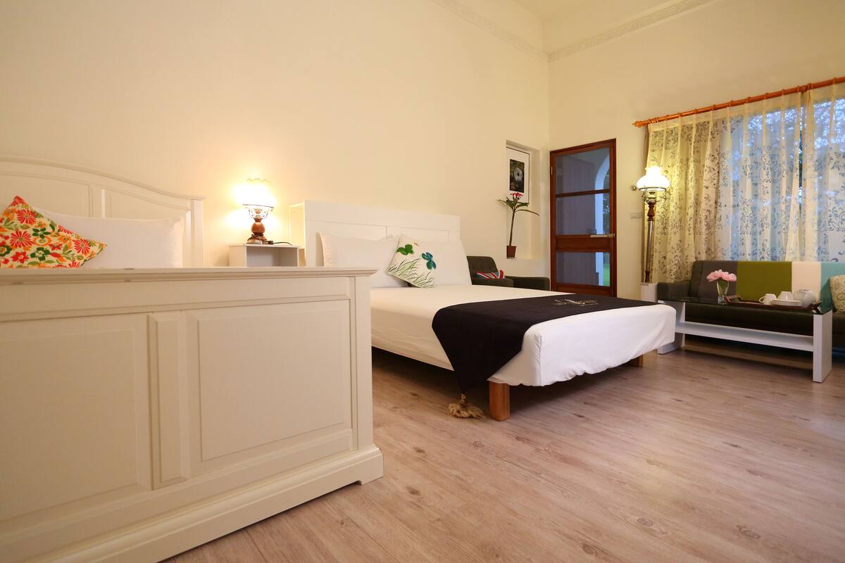 A bedroom with a bed, bedside table, lamp, and a window with curtains.