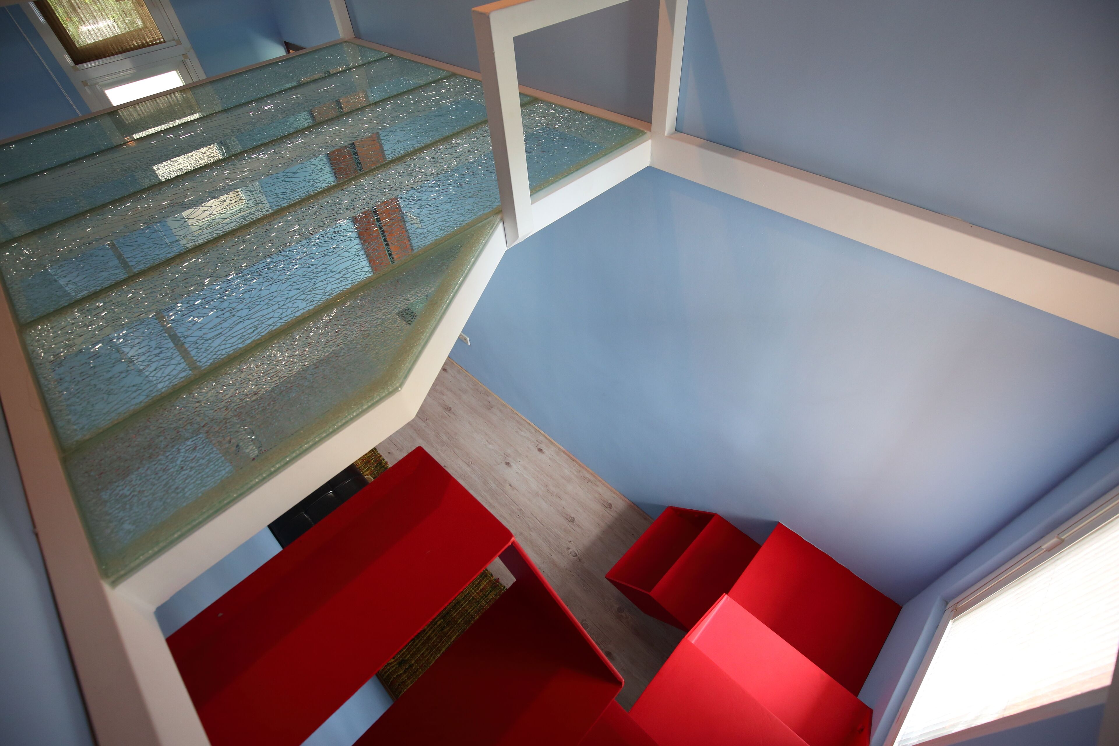 A modern interior with a glass staircase, red seating, and a blue wall.