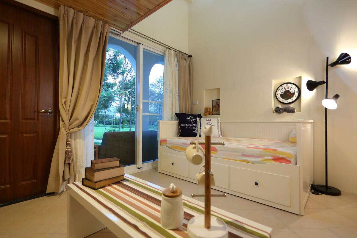 A bedroom with a bed, bedside table, lamp, and a view of the outdoors.