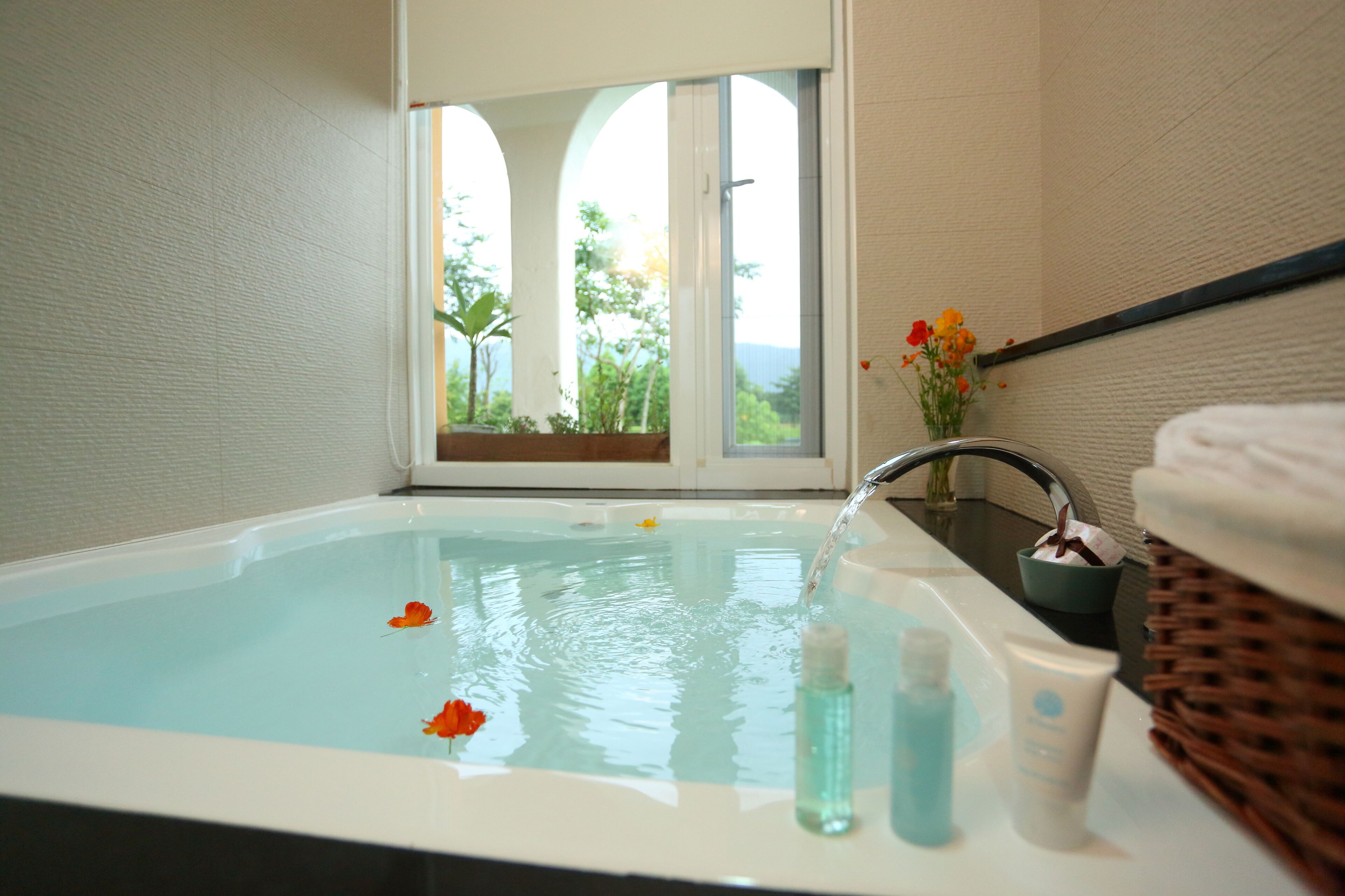 A bathroom with a bathtub, a window with a view of greenery, and toiletries on the counter.