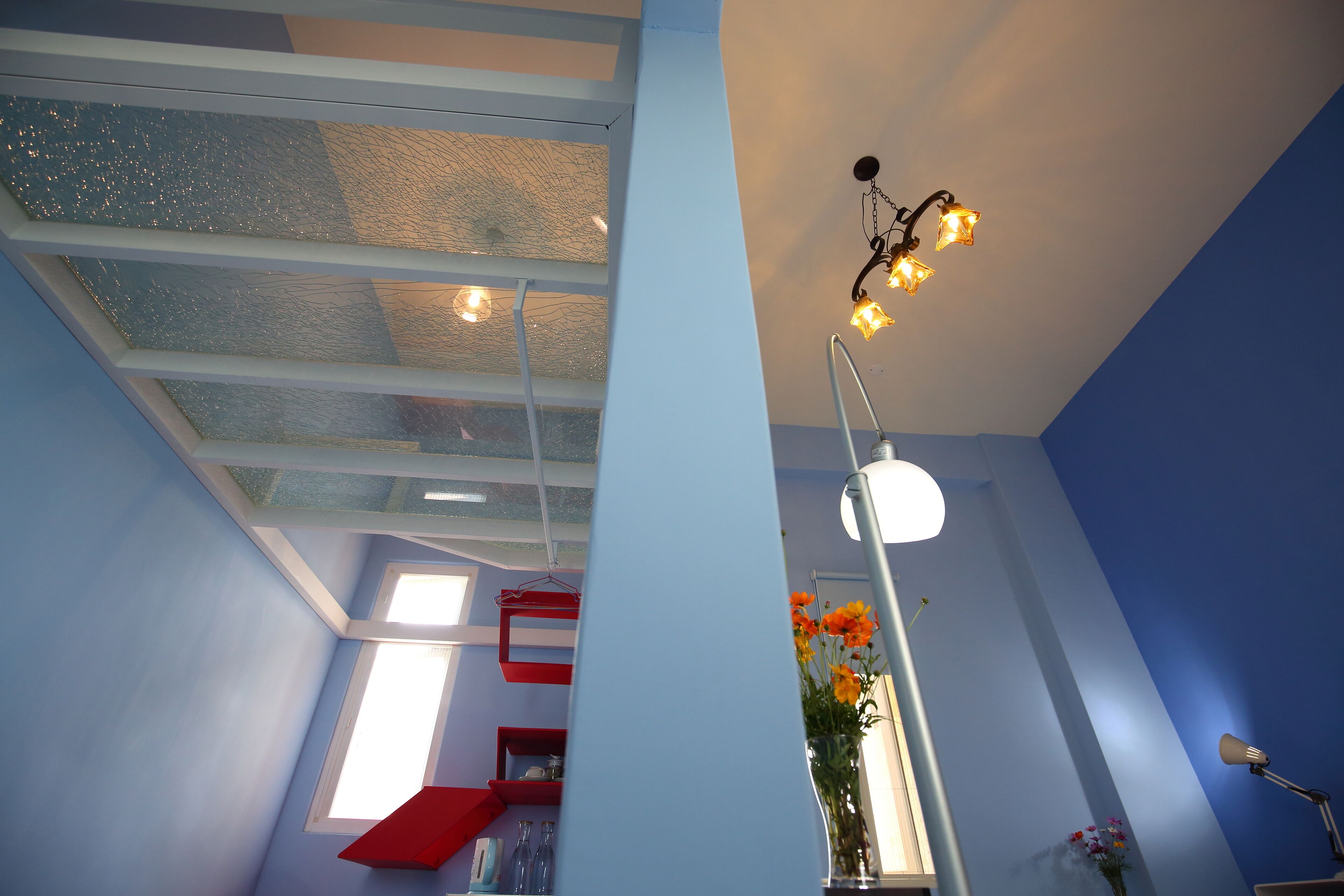 A room with a skylight, a red staircase, and a desk with a lamp and flowers.