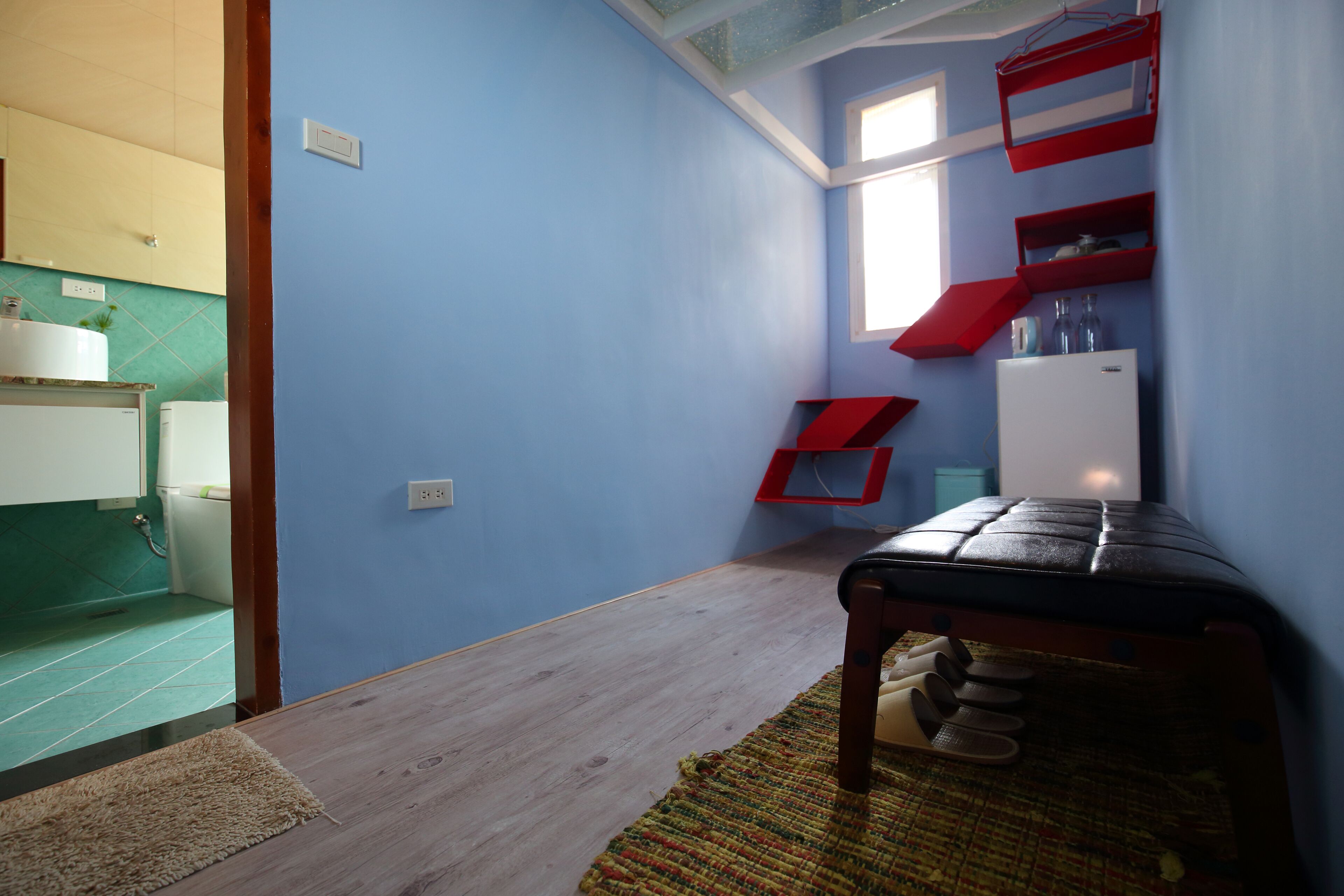 Una habitación pequeña con kitchenette, un banco de madera y un ventanal.