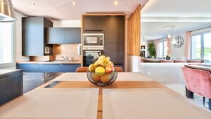 A modern kitchen with built-in appliances, a dining area with a central table, and a large window providing natural light. - MickeyRelax Luxury Spa Villa near Disneyland Paris (Villeneuve-Le-Comte)