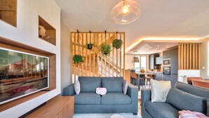 A modern living room with a grey sofa, a TV, and a wooden partition with hanging plants. - MickeyRelax Luxury Spa Villa near Disneyland Paris (Villeneuve-Le-Comte)