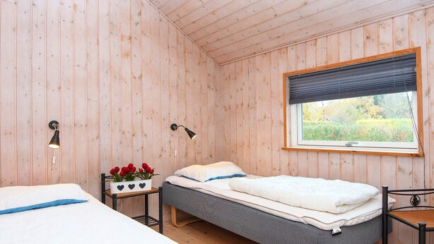 A room with two beds, a window with a view of greenery, and a small table with a plant. - 5 Star Holiday Home in Farvang (Farvang)