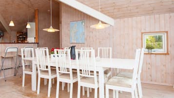 A dining area with a long table and white chairs, wooden walls, and hanging pendant lights.