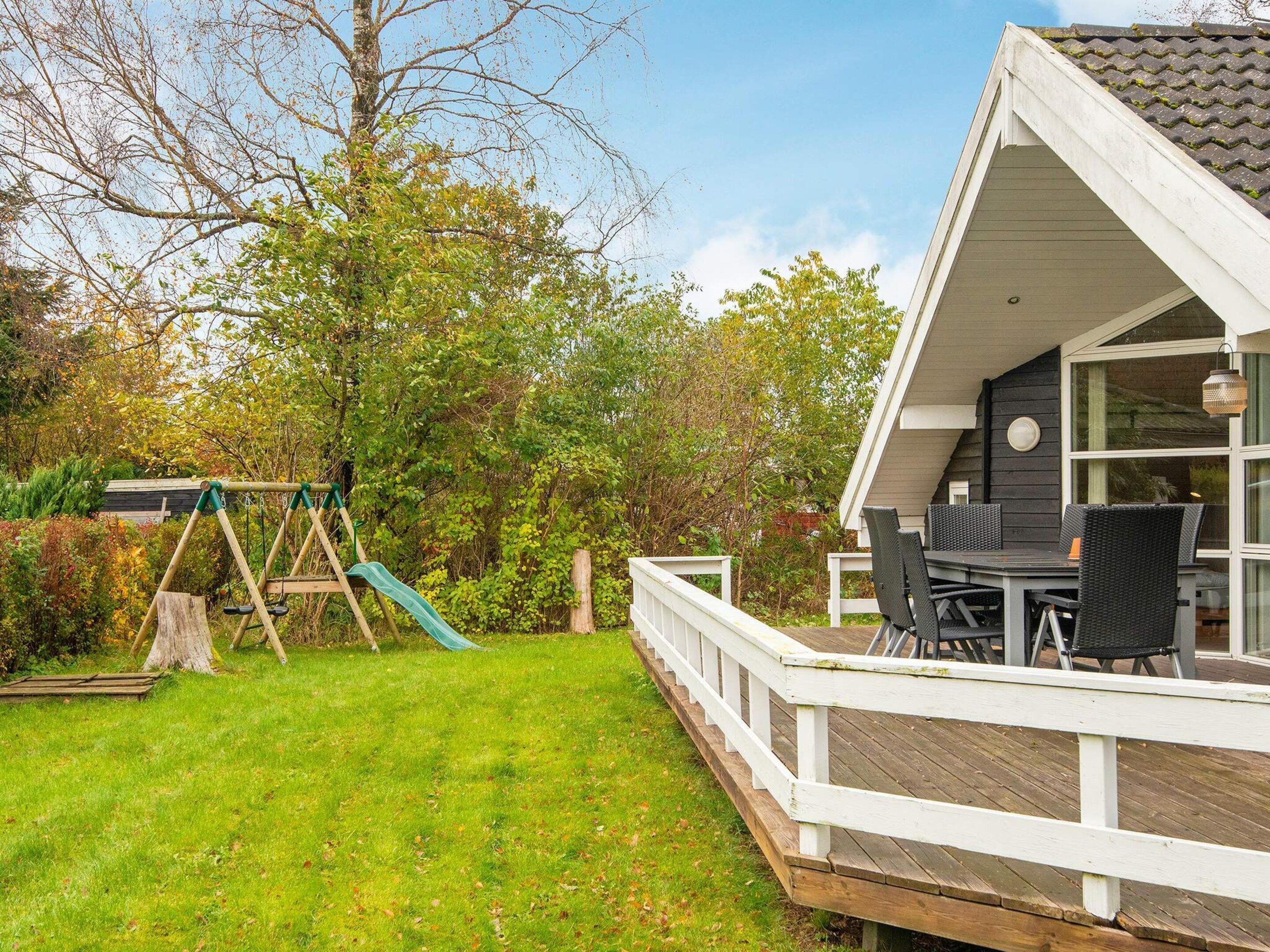 A residential property with a deck, a swing set, and a dining area with outdoor furniture.