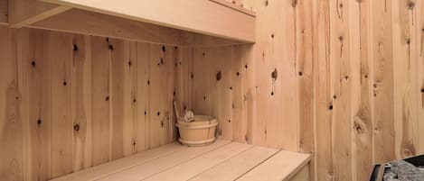 Un sauna de madera con un banco y un pequeño recipiente de madera.