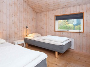 A room with wooden walls, a bed with a grey mattress, a bedside table with a lamp, and a window with a view of greenery. - 5 Star Holiday Home in Farvang (Farvang)