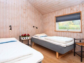 A wooden-paneled room with two beds, a small table with a plant, and a window with a view of greenery.