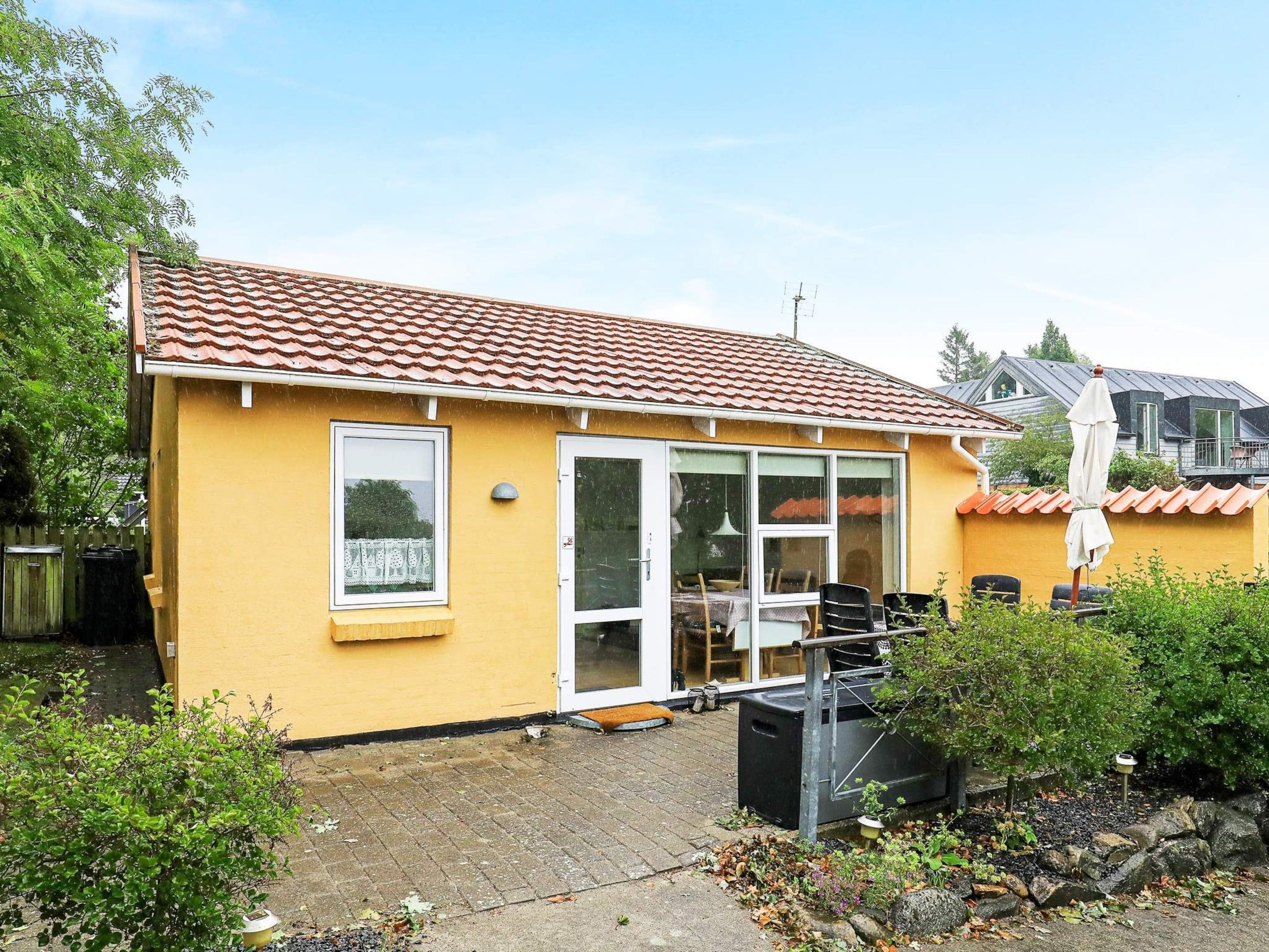 A yellow building with a tiled roof, a sliding glass door, and a patio area with outdoor furniture.