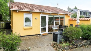 Een geel huis met een pannendak, een schuifdeur en een patio met tuinmeubilair.