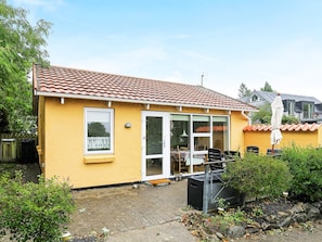 Ein gelbes Haus mit Ziegeldach, einer Schiebetür und einer Terrasse mit Gartenmöbeln.