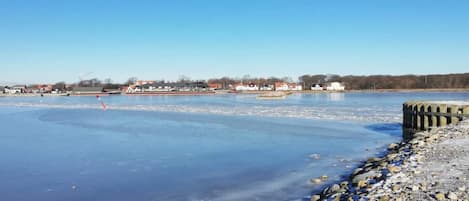 A frozen river with a rocky shoreline and buildings in the background.