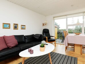 Ett modernt vardagsrum med en svart lädersoffa, ett vitt soffbord och en matplats med ett bord dukat för två personer.