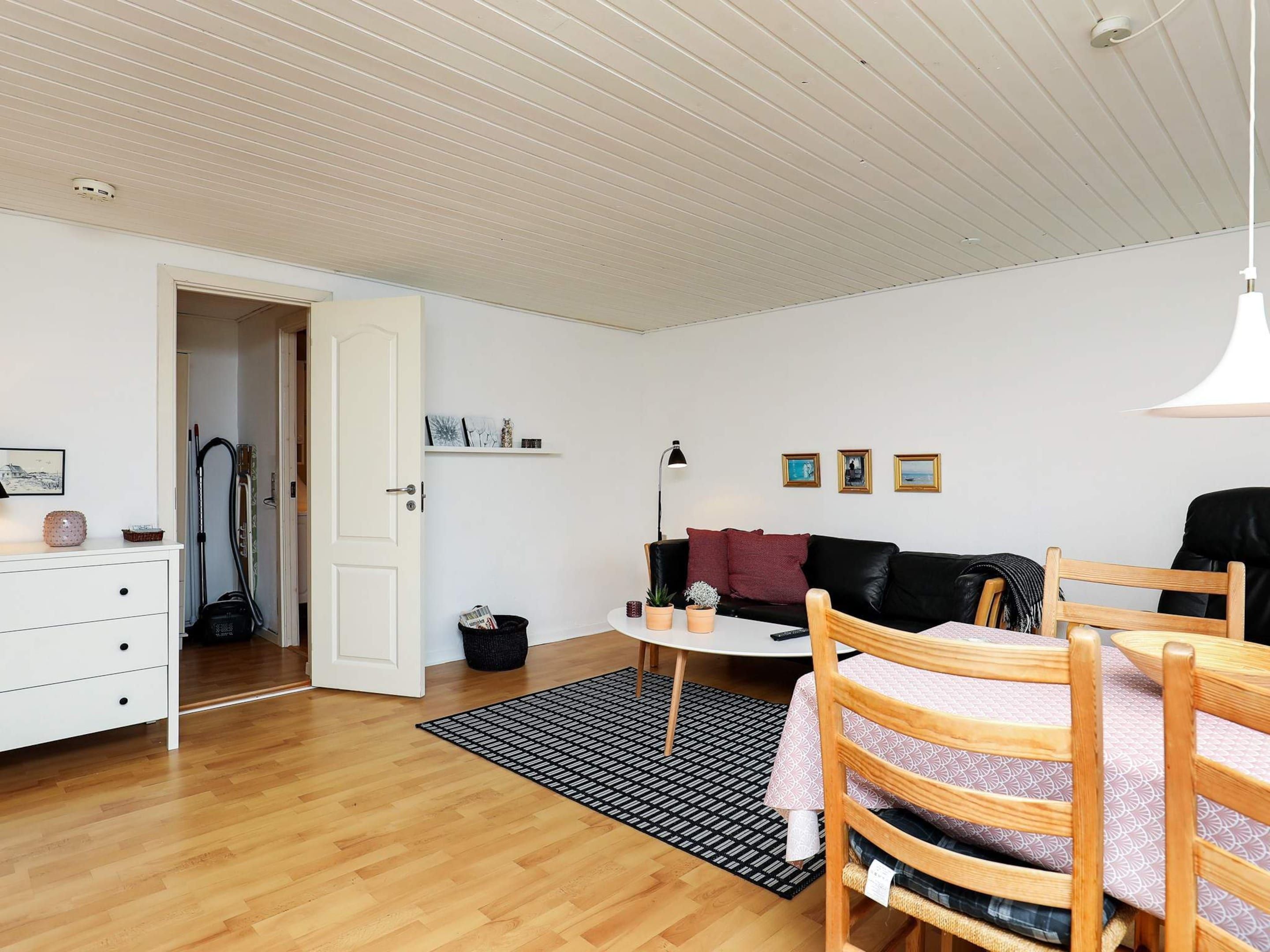 A room with a wooden floor, a black and white patterned rug, a white dresser, a black leather sofa, a small round table, and a wooden chair.