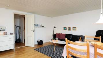 A room with a wooden floor, a black and white patterned rug, a white dresser, a black leather sofa, a small round table, and a wooden chair.