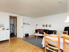 A room with a wooden floor, a black and white patterned rug, a white dresser, a black leather sofa, a small round table, and a wooden chair. - 4 Person Holiday Home in Nykobing M (Nykobing Mors)