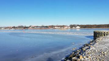 A frozen river with a rocky shore and buildings in the background.