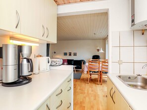 Cocina compacta con electrodomésticos modernos, comedor con mesa y sillas de madera, y un lavamanos visible.