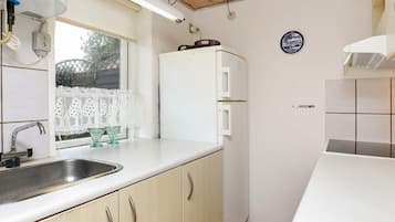 A compact kitchen with a sink, a refrigerator, and a window with lace curtains.