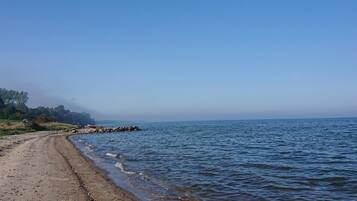A beach with a clear sky, a rocky shoreline, and a calm sea.